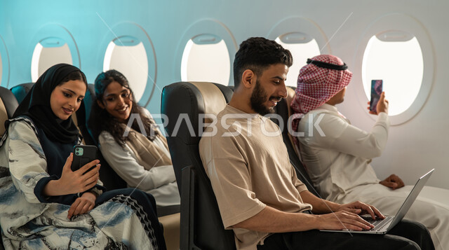 مجموعة من الشباب والبنات العرب الخليجيون السعوديون في الطائرة ، التقاط  صور تذكارية باستخدام الهاتف المحمول ،  رحلة جوية سياحية ممتعة برفقة الاصدقاء ، عطلة صيفية سعيدة ، الخطوط الجوية السعودية.