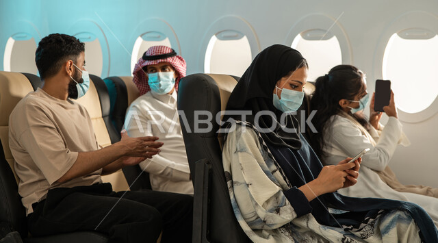 مجموعه من المسافرين العرب الخليجيين السعوديين في مقصورة الطائرة ،  ارتداء الكمامة الطبية ، التباعد الاجتماعي ، اجراءات الوقاية من فايروس كورونا ، الخطوط الجوية السعودية ، دردشة ومحادثات.