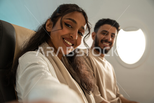 امرأة ورجل عربيان خليجيان سعوديان في مقصورة الطائرة ، ايماءات تدل على الفرح والسعادة ، رحلات سياحية جويه ممتعة ، عطلة صيفية عائلية ، الخطوط الجوية السعودية ، سياحة وسفر.