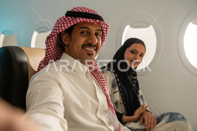 زوجان عربيان سعوديان خليجيان  في مقصورة  الطائرة ، ايماءات تدل على السعادة والسرور  ، قضاء أوقات ممتعة داخل الطائرة ، عطلة صيفية عائلية ، الخطوط الجوية السعودية ، سياحة وسفر.