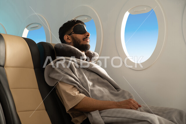 ايماءات تدل على النوم والاسترخاء ، رجل عربي خليجي سعودي يرتدي اللباس الكاجوال يجلس في مقصورة الطائرة ،  الشعور بالتعب والارهاق ، وسائل مواصلات جوية ، خطوط الطيران الجوي ، سياحة وسفر ، رحلات جوية سياحية.
