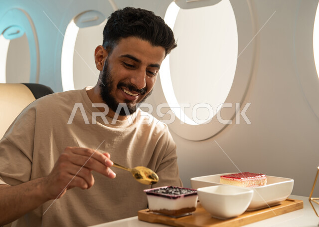 صورة مقربة لشاب سعودي عربي  يرتدي اللباس الكاجوال  يستمتع بالوجبة المقدمة على متن الطائرة ، الخطوط الجوية السعودية ، ايماءات تدل على السعادة والسرور ، سياحة وسفر ، رحلة عمل ، رحلات جوية سياحية.