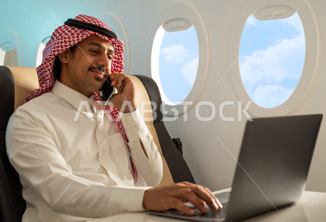  درجة رجال الاعمال ، رجل عربي خليجي سعودي يرتدي الزي السعودي التقليدي يجلس في مقعد الطائرة ، انجاز مهام العمل في مقصورة الطائرة ، اجراء مكالمة هاتفية ، استخدام  الحاسوب المحمول ، رحلة عمل ، الخطوط الجوية السعودية.