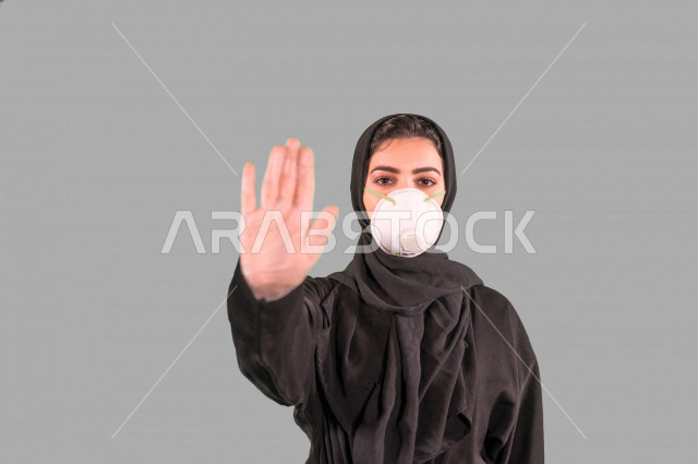 بورتريه لمرأة عربية خليجية سعودية ترتدي الكمامة والقفازات الواقية، اتخاذ اجراءات الوقاية من فايروس كورونا (كوفيد-19)، امرأة ترفع يدها لتجنب اقتراب الاخرين منها، الحفاظ على المسافات، خلفية بيضاء