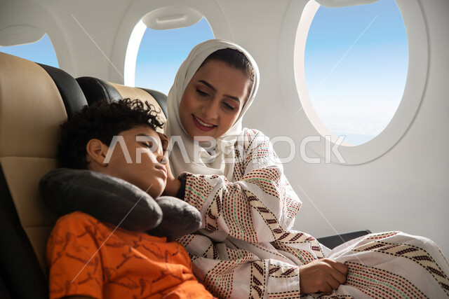 A family tourist trip, a Saudi Arabian Gulf woman accompanied by her sleeping son on the plane, feeling tired and exhausted and the need for sleep and rest, spending the summer vacation with the family, Saudi Airlines