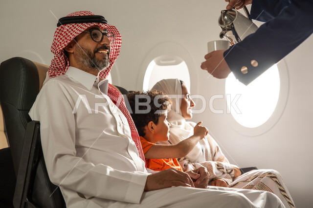 قضاء العطلة الصيفية برفقة العائلة، صورة مقربة ليد مضيفة الطيران تقوم بتقديم المشروبات الساخنة لركاب الطائرة، عائلة عربية خليجية سعودية في الطائرة، حسن الضيافة والاستقبال، رحلة سياحية عائلية، خطوط الطيران السعودي