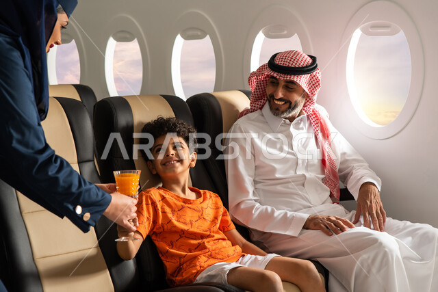 مضيفة الطيران تقوم بتقديم العصير لولد عربي خليجي سعودي برفقة والده في رحلة سياحية في الطائر، حسن الضيافة والاستقبال، ايماءات وجه تدل على السعادة، خطوط الطيران السعودي
