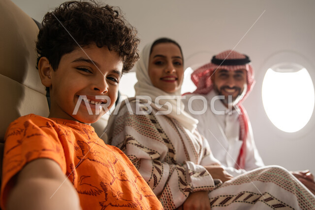 A family tourist trip, spending the summer vacation with the family, a happy Saudi Gulf Arab family on a tourist trip in the plane, facial gestures indicating happiness, Saudi Airlines