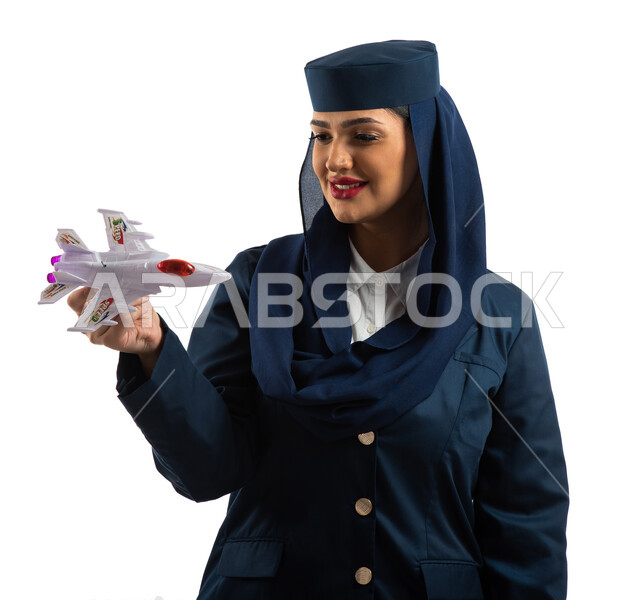 بورتريه لمضيفة طيران عربية سعودية خليجية مبتسمة ترتدي زي مضيفات الطيران و تحمل مجسم مصغر لطائرة ، خطوط الطيران السعودي مهنة مضيفة الطيران ، طاقم الطائرة ، خلفية بيضاء.