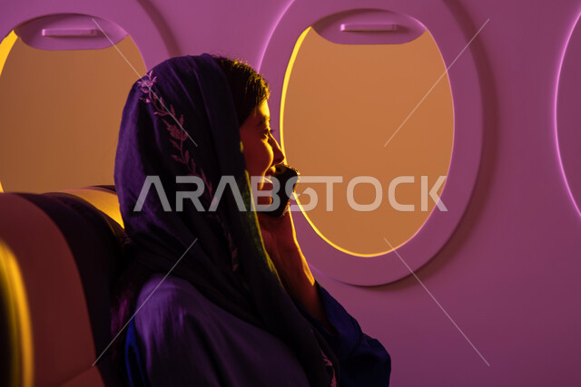 اجراء مكالمات عبر الهاتف المحمول, محادثات ودردشة, تواصل اجتماعي ,فتاة عربية خليجية سعودية محجبة في مقعد الطائرة ، رحلات جوية سياحية ، ايماءات تدل على الفرح والسرور , عطلة صيفية سعيدة, خطوط الطيران السعودي ،رحلة عمل.