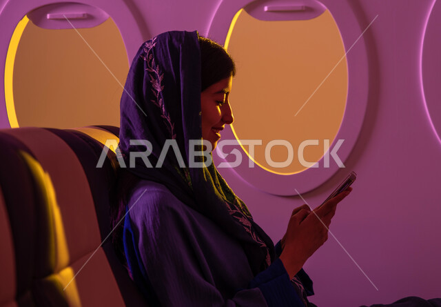 محادثات ودردشة, تواصل اجتماعي ,فتاة عربية خليجية سعودية محجبة في مقعد الطائرة ، رحلات جوية سياحية ، استخدام الهاتف المحمول ، تصفح الانترنت ، ايماءات تدل على السعادة, عطلة صيفية سعيدة, خطوط الطيران السعودي ،رحلة عمل.