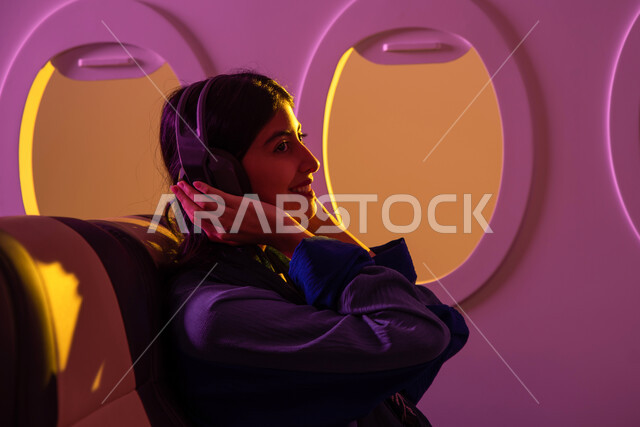 الاستمتاع بالعطلة الصيفية , سفر وسياحة, ايماءات تدل على الفرح والراحة, فتاة عربية خليجية سعودية محجبة تجلس في مقعد الطائرة, استخدام تقنية الهيدفون, رحلات جوية سياحية, الخطوط الجوية السعودية, رحلة عمل .