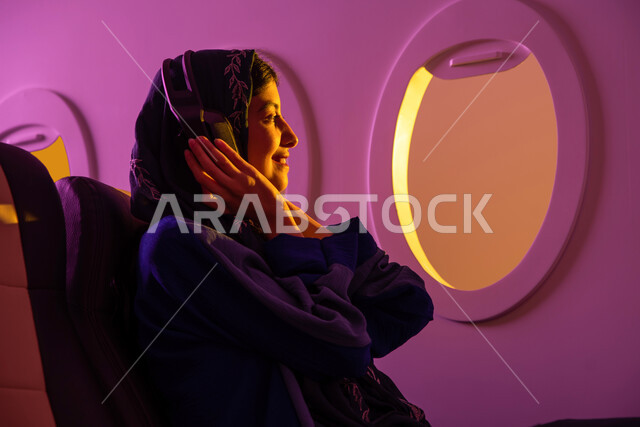 الاستمتاع بالعطلة الصيفية , سفر وسياحة, ايماءات تدل على الفرح والراحة, امرأة عربية خليجية سعودية محجبة تجلس في مقعد الطائرة, استخدام تقنية الهيدفون, رحلات جوية سياحية, الخطوط الجوية السعودية, رحلة عمل .