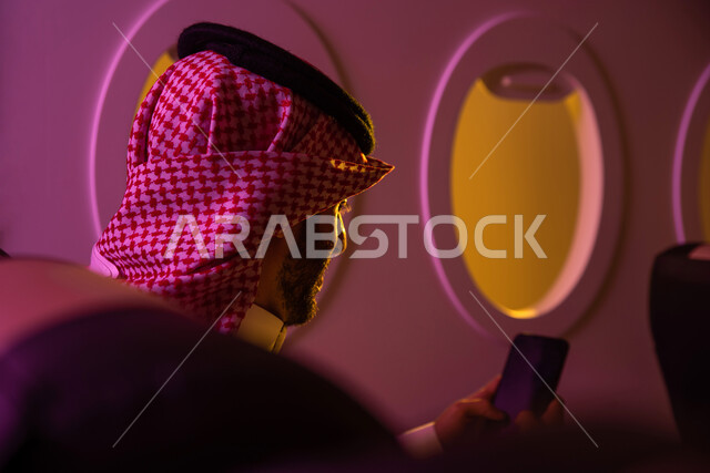 Happy summer vacation, social networking via mobile phone, a picture from the back of a Saudi Arabian Gulf man wearing traditional Saudi dress and sitting in the seat of the plane, chat and conversations, tourism and travel, tourist flights, Saudi Airline