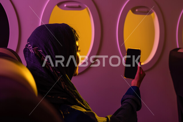 تواصل اجتماعي ,صورة من الخلف لفتاة عربية خليجية سعودية محجبة في مقعد الطائرة ، رحلات جوية سياحية ، استخدام الهاتف المحمول ، تصفح الانترنت ، خطوط الطيران السعودي  ،رحلة عمل.