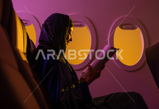  قراءة الكتب المفيدة للتعلم والتثقف, ممارسة هواية القراءة ، امرأة عربية خليجية سعودية ترتدي العباءة الخليجية تجلس في مقعد الطائرة ، قضاء أوقات ممتعة في مقصورة الطائرة  ، رحلة عمل ، خطوط الطيران السعودي.