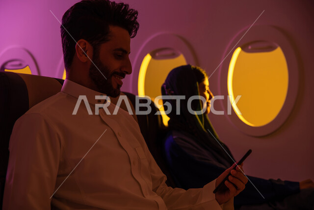 سياحة وسفر, عطلة صيفية سعيدة, ايماءات تدل على الفرح والسعادة, رجل وامرأه عربيان سعوديان خليجيان في مقعد الطائرة, دردشة ومحادثات  عن طريق الهاتف المحمول ,الخطوط الجوية السعودية, رحلة عمل, رحلات جوية سياحية .