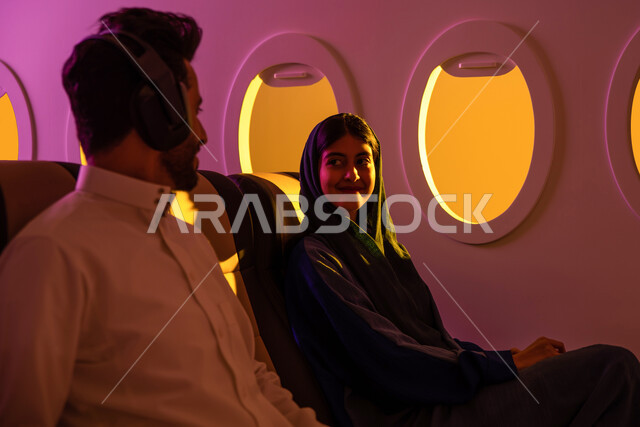 عطلة صيفية سعيدة, زوجان عربيان سعوديان خليجيان في مقعد الطائرة, ايماءات تدل على السعادة والفرح, دردشة ومحادثات,  استخدام تقنية الهيدفون, درجة رجال أعمال, الخطوط الجوية السعودية, رحلة عمل, سياحة وسفر, رحلات جوية سياحية .