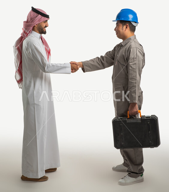 بورتريه لمهندس معماري فلبيني يرتدي الخوذة الواقية ويصافح رجل عربي خليجي سعودي، الزي السعودي التقليدي، التحية والسلام، صداقة وتعارف، عامل بناء يحمل حقيبة العدة اليدوية، استقدام العمالة من الخارج، صورة الجسم بالطول الكامل، خلفية بيضاء