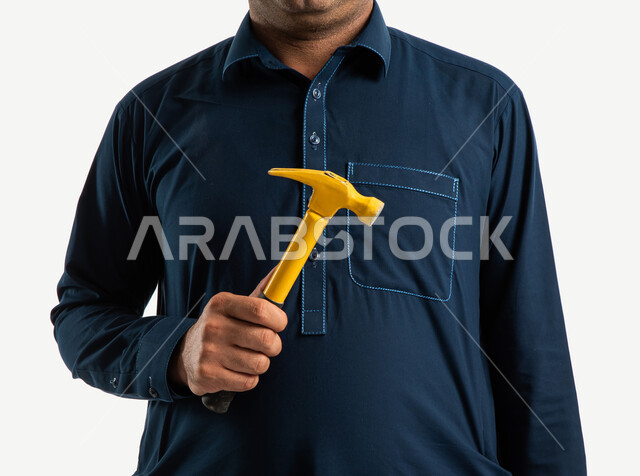صورة مقربة لعامل بناء باكستاني يرتدي الزي الباكستاني التقليدي ويمسك بمطرقة معدنية، ادوات البناء والنجارة، مقبض بلاستيكي، شاكوش، بورتريه لمهندس معماري، ادوات التشطيب، استقدام العمالة من الخارج، خلفية بيضاء