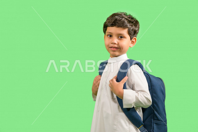كروما لطالب مدرسي عربي خليجي سعودي يرتدي حقيبة ظهر مدرسية، ارتداء الزي المدرسي التقليدي، ايماءات وجه ويدين تدل على السعادة، خلفية خضراء