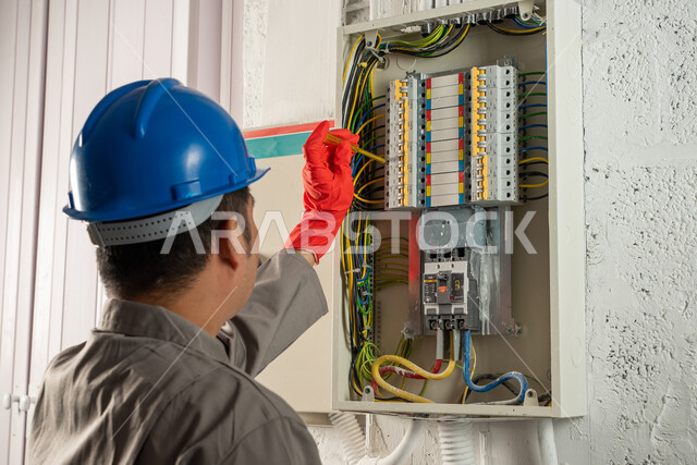 عامل صيانة كهربائي يرتدي خوذة الحماية وقفازات العزل الكهربائي ويستخدم مفك فحص الكهرباء، صيانة وتركيب لوحة عداد الكهرباء، مفهوم الهندسة الكهربائية، تركيب مفاتيح الكهرباء، عمل فني كهربائي، تمديد اسلاك الكهرباء، استقدام العمالة من الخارج