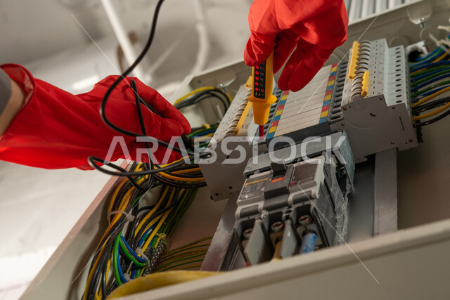 عامل صيانة كهربائي يرتدي قفازات العزل الكهربائية ويستخدم جهاز قياس التيار الكهربائي (الأميتر)، صيانة وتركيب لوحة عداد الكهرباء، مفهوم الهندسة الكهربائية، تركيب مفاتيح الكهرباء، عمل فني كهربائي، تمديد اسلاك الكهرباء، استقدام العمالة من الخارج