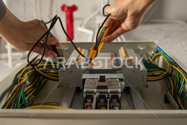 A close-up of an electric technician's hand using an ammeter, maintenance and installation of the electricity meter board, the concept of electrical engineering, installation of electric switches, electrical technician work, extension of electrical wires,