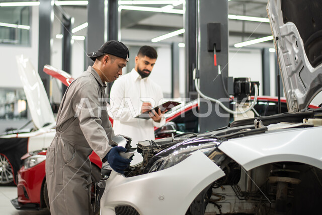 معامل و ورش الصيانه في المملكه العربيه السعوديه,  مهندس ميكانيكي محترف, تسجيل و تدوين الملاحظات , صوره مقربه لعامل صيانه فلبيني يقوم بإصلاح سيارة عميل عربي سعودي خليجي في الورشه, التشييك وتصليح السيارات في مركز الصيانه