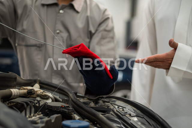 فحص منسوب زيت محرك السيارة, ورش ومعامل الصيانه في المملكه العربيه السعوديه, التشييك وتصليح السيارات في مركز الصيانه, صوره مقربه لعامل صيانه يقوم بإصلاح سيارة عميل عربي سعودي خليجي في الورشه, مهندس ميكانيكي محترف