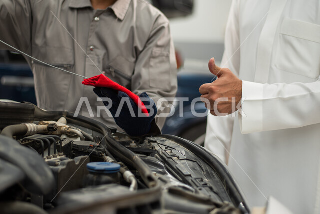 ايماءات يد تدل على علامة الجودة, مهندس ميكانيكي محترف, فحص منسوب زيت محرك السيارة, ورش ومعامل الصيانه في المملكه العربيه السعوديه, التشييك وتصليح السيارات في مركز الصيانه, صوره مقربه لعامل صيانه يقوم بإصلاح سيارة عميل عربي سعودي خليجي في الورشه
