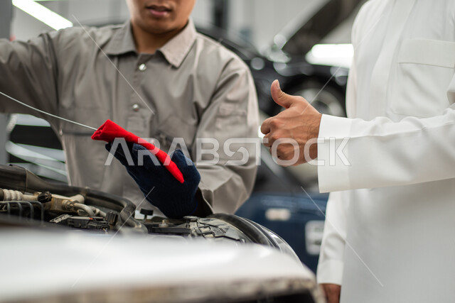 ايماءات يد تدل على علامة الجودة, مهندس ميكانيكي محترف, فحص منسوب زيت محرك السيارة, ورش ومعامل الصيانه في المملكه العربيه السعوديه, التشييك وتصليح السيارات في مركز الصيانه, صوره مقربه لعامل صيانه يقوم بإصلاح سيارة عميل عربي سعودي خليجي في الورشه