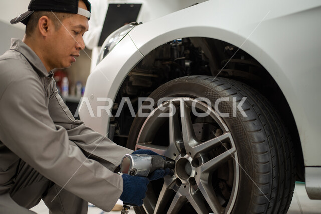A close-up of a mechanical maintenance worker who inflates and repairs car wheels, using appropriate maintenance tools, distinguished manual repair, repairing a Saudi Arabian Gulf customer’s car in the workshop, checking and repairing cars in the maintena