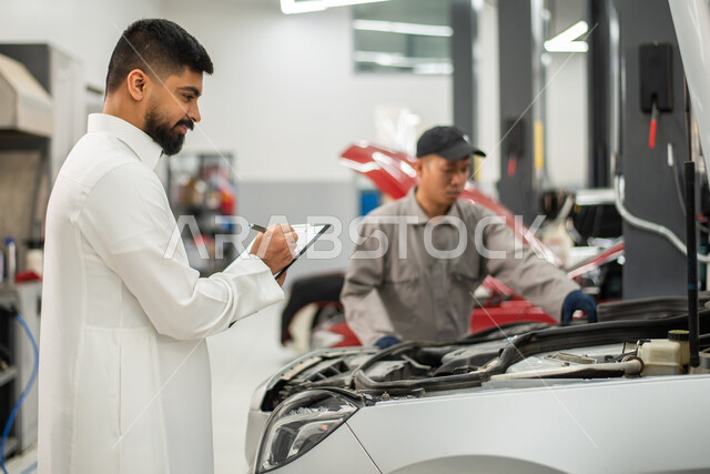 Taking and writing notes, maintenance workshops and laboratories in the Kingdom of Saudi Arabia, a close-up of a Filipino maintenance worker who repairs a car for a Saudi Arabian Gulf customer in the workshop, checks and car repairs in the maintenance cen