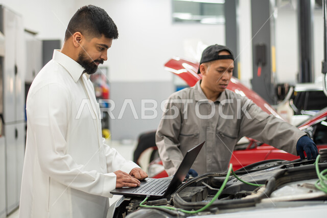 طلب تصليح السياره عن طريق جهاز الحاسوب المحمول, صوره مقربه لعامل صيانه فلبيني يقوم بإصلاح سيارة عميل عربي سعودي خليجي في الورشه, ايماءات تدل على الرضا والقبول بخدمات الورشه, التشييك وتصليح السيارات في مركز الصيانه, مهندس ميكانيكي محترف