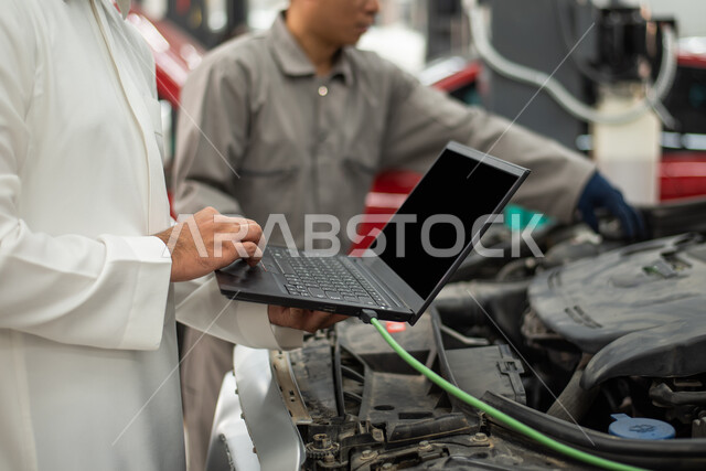 ورش ومعامل الصيانه في المملكه العربيه السعوديه, التشييك وتصليح السيارات في مركز الصيانه, طلب تصليح السياره عن طريق جهاز الحاسوب المحمول, صوره مقربه لعامل صيانه يقوم بإصلاح سيارة عميل عربي سعودي خليجي في الورشه,  مهندس ميكانيكي محترف