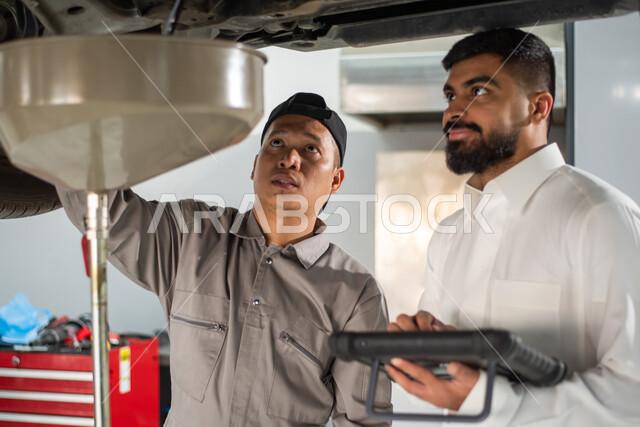  طلب تصليح السيارة عن طريق جهاز التابلت, التشييك وتصليح السيارات في مركز الصيانه, صوره مقربه لعامل صيانه فلبيني يقوم بإصلاح سيارة عميل عربي سعودي خليجي في الورشه, ايماءات تدل على الرضا والقبول بخدمات الورشه, مهندس ميكانيكي محترف