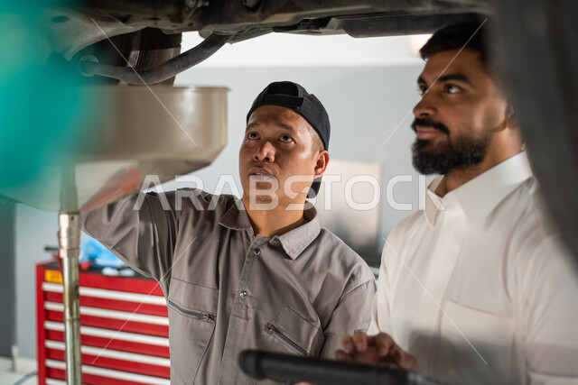 التشييك وتصليح السيارات في مركز الصيانه, طلب تصليح السيارة عن طريق جهاز التابلت, صوره مقربه لعامل صيانه فلبيني يقوم بإصلاح سيارة عميل عربي سعودي خليجي في الورشه, ايماءات تدل على الرضا والقبول بخدمات الورشه, مهندس ميكانيكي محترف