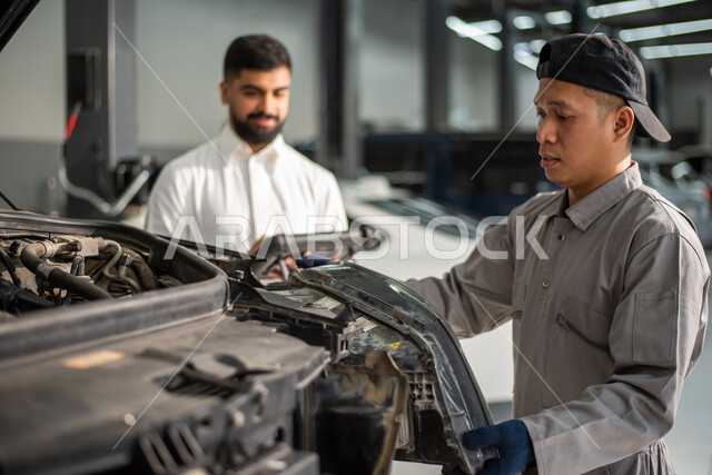 مهندس ميكانيكي محترف, طلب تصليح السياره عن طريق جهاز التابلت, صوره مقربه لعامل صيانه فلبيني يقوم بإصلاح سيارة عميل عربي سعودي خليجي في الورشه, ايماءات تدل على الرضا والقبول بخدمات الورشه, التشييك وتصليح السيارات في مركز الصيانه