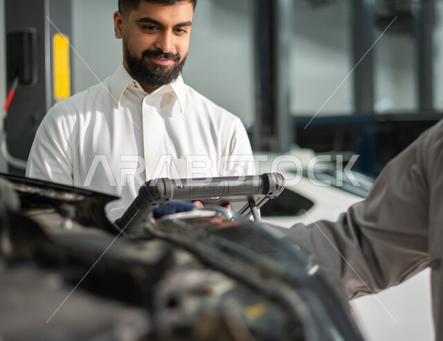 طلب تصليح السياره عن طريق جهاز التابلت, صوره مقربه لعامل صيانه يقوم بإصلاح سيارة عميل عربي سعودي خليجي في الورشه, ايماءات تدل على الرضا والقبول بخدمات الورشه, التشييك وتصليح السيارات في مركز الصيانه, مهندس ميكانيكي محترف