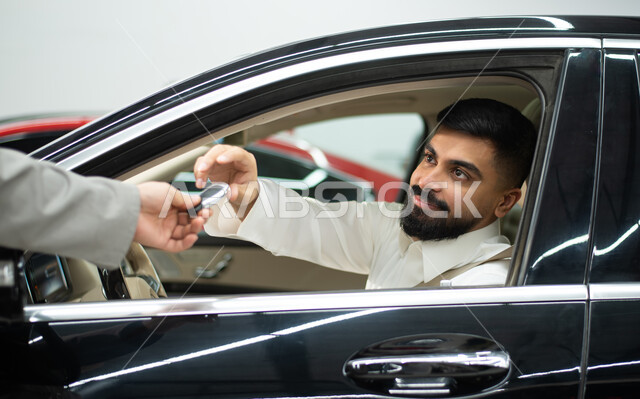  مركز الصيانه وتصليح وسائل المواصلات, ايماءات تدل على القبول والرضى عن الخدمات الراقية و المتميزة, خدمات اصلاح وصيانة السيارات في الورشه, سائق عربي سعودي خليجي مبتسم يرتدي الثوب السعودي التقليدي يجلس في السياره يقوم بتسليم مفتاح السيارة لعامل الصيانة 