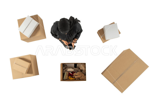 مندوبة توصيل الطلبات والبضائع للزبائن، امينة مستودع تستخدم الهاتف المحمول، تغليف صناديق الطلبات، صورة علوية عامودية لامرأة سعودية، التسويق الالكتروني الذكي، التشيك على الحجوزات، خدمات الشحن والتوصيل، خلفية بيضاء