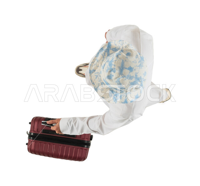 شاب سعودي خليجي يرتدي قبعة كاجوال ويستعد لقضاء الاجازة الصيفية، صورة علوية عامودية لرجل عربي خليجي سعودي يسمك بيده حقيبة السفر، الاستعداد للسفر والسياحة، الذهاب في رحلة سياحية ممتعة، خلفية بيضاء