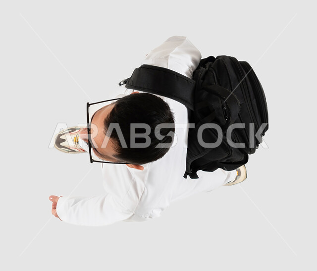 A young Saudi Gulf man carrying his personal backpack and getting ready to spend the summer vacation, a vertical overhead image of a Saudi Arab Gulf man wearing sunglasses, getting ready for travel and tourism, going on an enjoyable tourist trip, a gray b