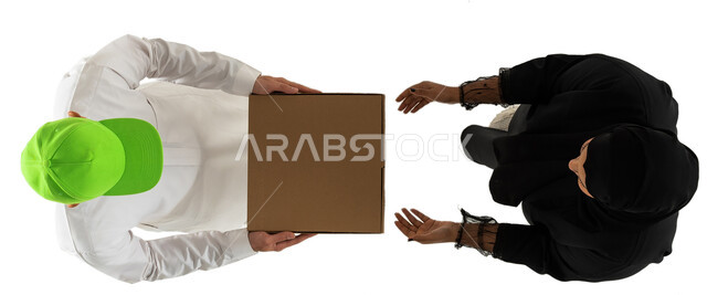 امرأة تستلم الطلب من مندوب توصيل يرتدي قبعة خضراء، عملية شحن وتوصيل موثوقه وناجحة، صورة علوية عامودية لرجل وامرأة عربيان خليجيان سعوديان يرتديان الزي السعودي التقليدي، تسليم الطلبات للزبائن، خدمات التوصيل السريع، خلفية بيضاء