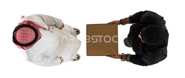 امرأة تقوم باستلام الطلب من مندوب التوصيل، صورة علوية عامودية لرجل وامرأة عربيان خليجيان سعوديان يرتديان الزي السعودي التقليدي، تسليم الطلبات للزبائن، عملية شحن وتوصيل موثوقه وناجحة، خدمات التوصيل السريع، خلفية بيضاء