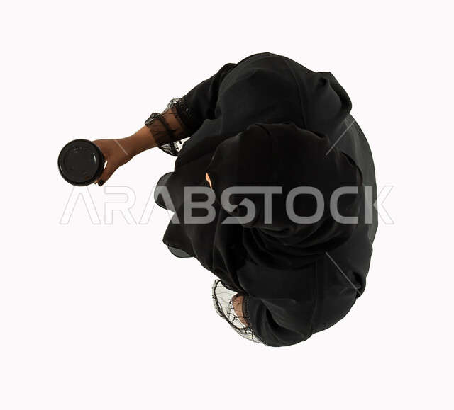 التسوق الالكتروني الذكي والطلبات الاونلاين، صورة علوية عامودية لامرأه عربية سعودية خليجية تحمل كوب القهوة، استلام المشتريات والطلبات، عملية شراء وتوصيل موثوقة، خدمات التوصيل السريع للمشروبات الساخنة، خلفية بيضاء