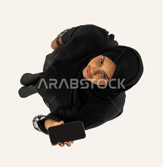 A mobile phone with a blank black screen, a vertical top image of a Saudi Arab Gulf woman, displaying mobile services and applications, e-shopping, happy face gestures, white background