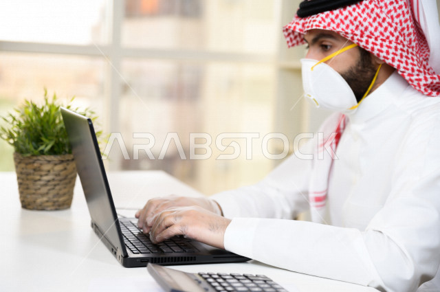 رجل اعمال عربي سعودي خليجي يرتدي الكمامة والقفازات لضبط انتشار العدوى ، استخدام الحاسوب المحمول لانجاز العمل ، القيام بالعمليات المحاسبية ، العمل عن بعد ، اجتماعات اونلاين ، التسويق الالكتروني