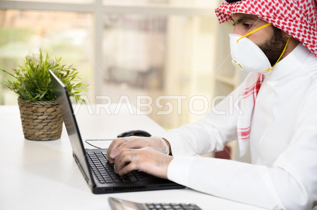 رجل اعمال عربي سعودي خليجي يرتدي الكمامة والقفازات لضبط انتشار العدوى ، استخدام الحاسوب المحمول لانجاز العمل ، القيام بالعمليات المحاسبية ، العمل عن بعد ، اجتماعات اونلاين ، التسويق الالكتروني